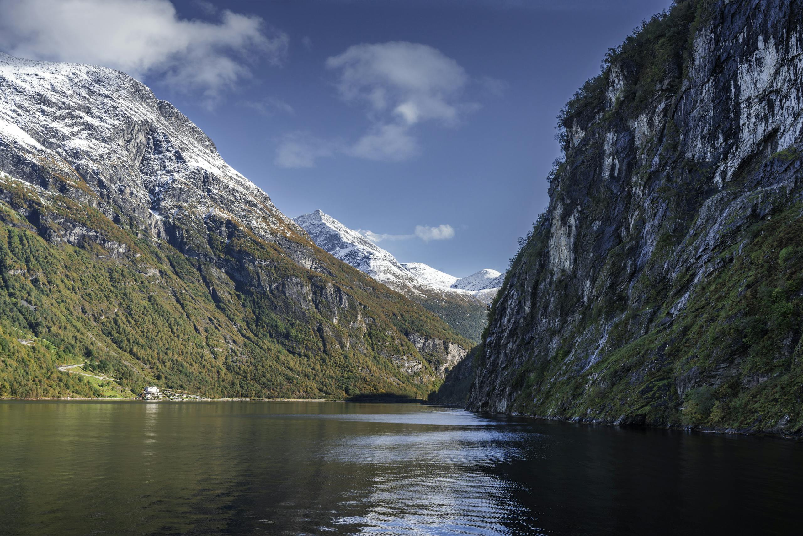 Breathtaking view of a Norwegian fjord with snow-capped mountains and clear blue skies.