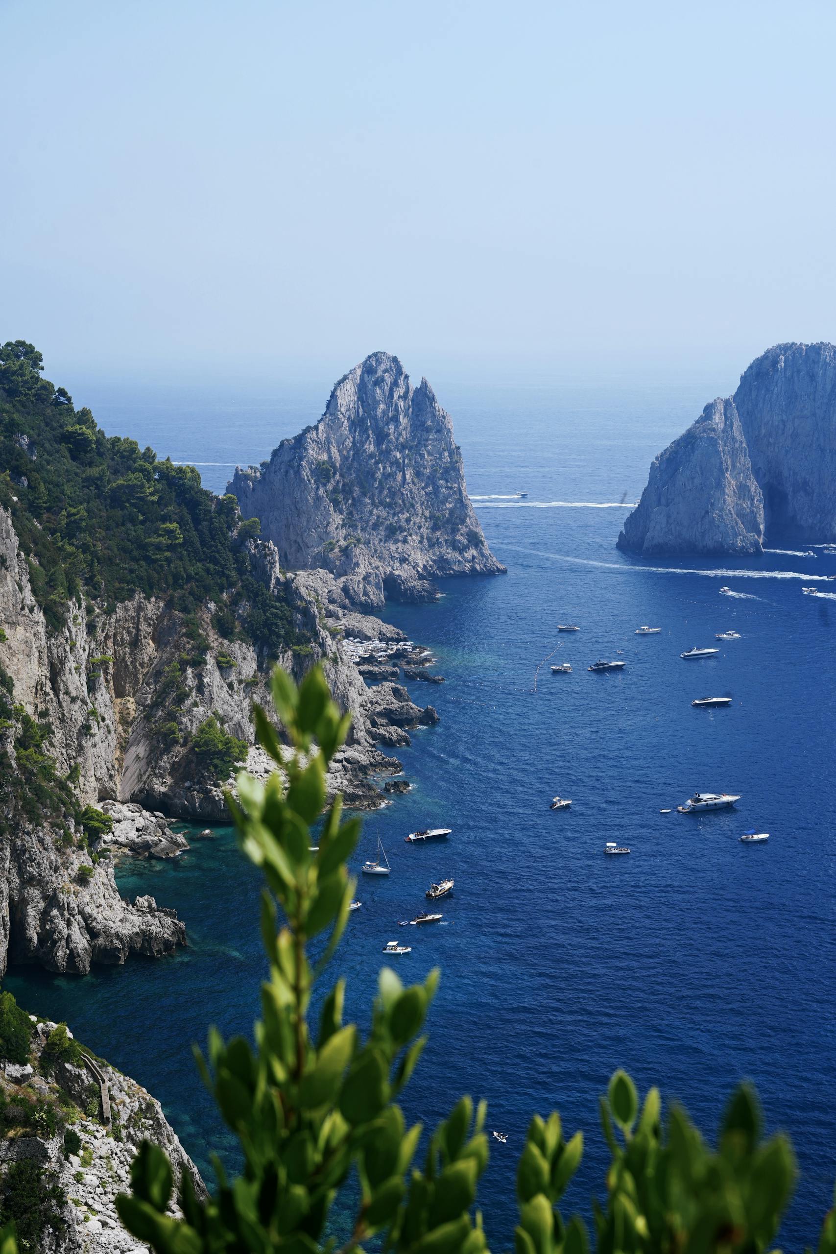 Majestic view of Capri's coastline and iconic rock formations with boats on the clear blue sea.