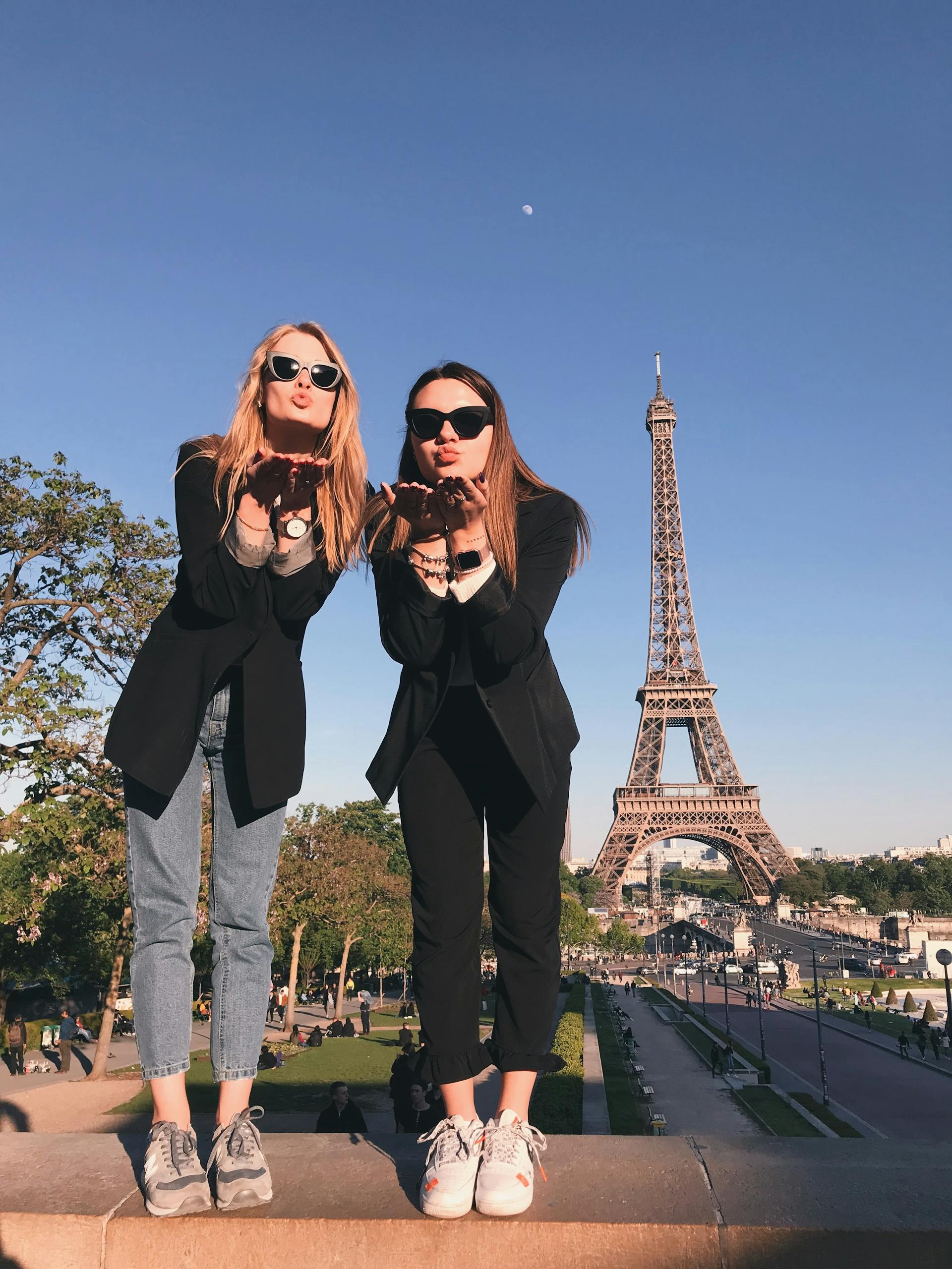 Two stylish women pose in front of the Eiffel Tower in Paris, symbolizing friendship and travel.
